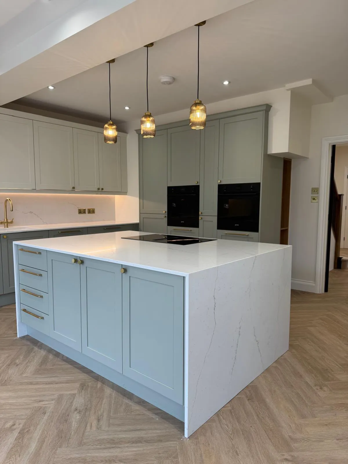 Sage green shaker kitchen with a marble-effect waterfall island and brass pendant lights