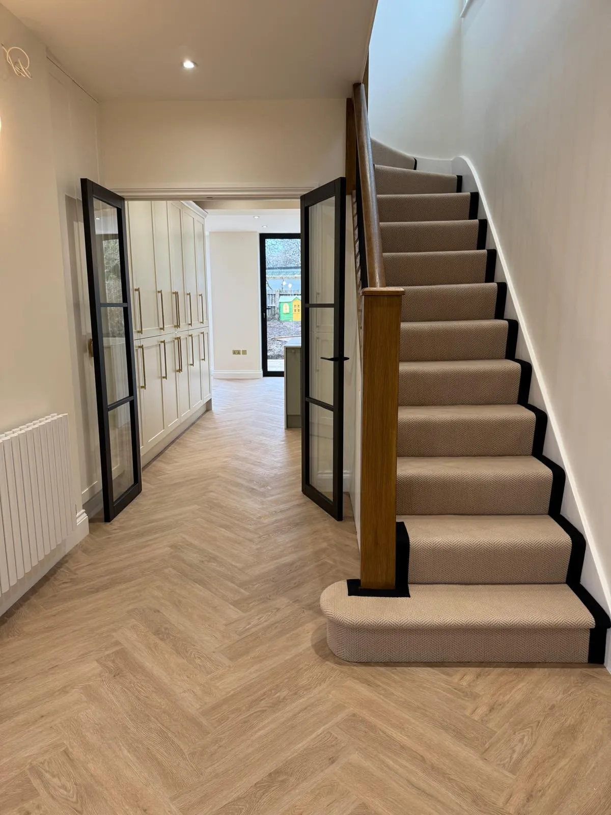 Hallway with herringbone flooring, oak staircase and black glazed doors