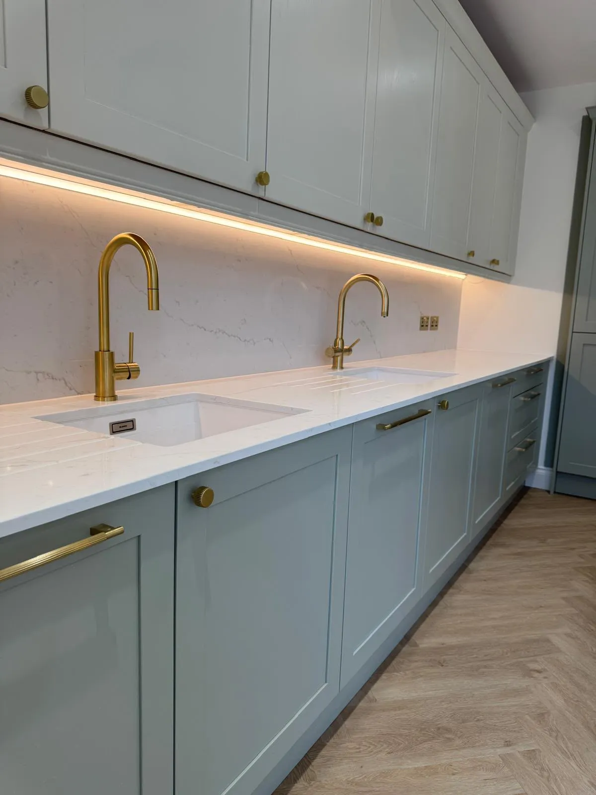 Kitchen worktop with two sinks, brass taps and under-cabinet lighting