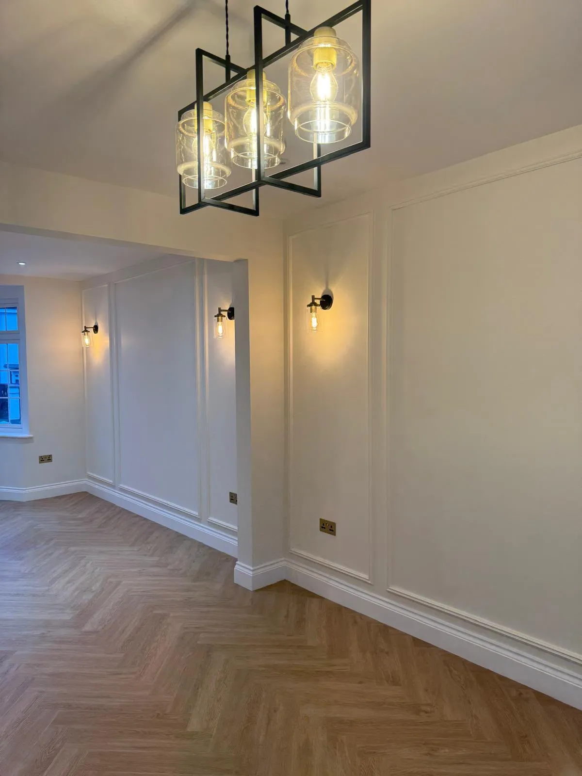 Living room with wall panelling, wall lights and herringbone floor