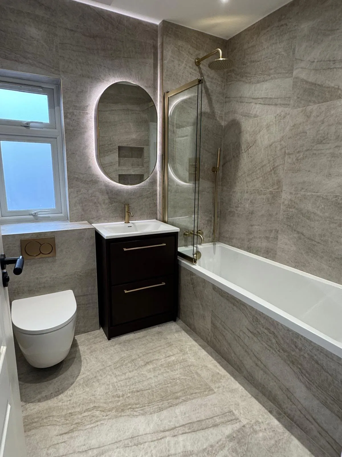 Bathroom with stone-effect tiles, illuminated oval mirror and brushed brass fittings