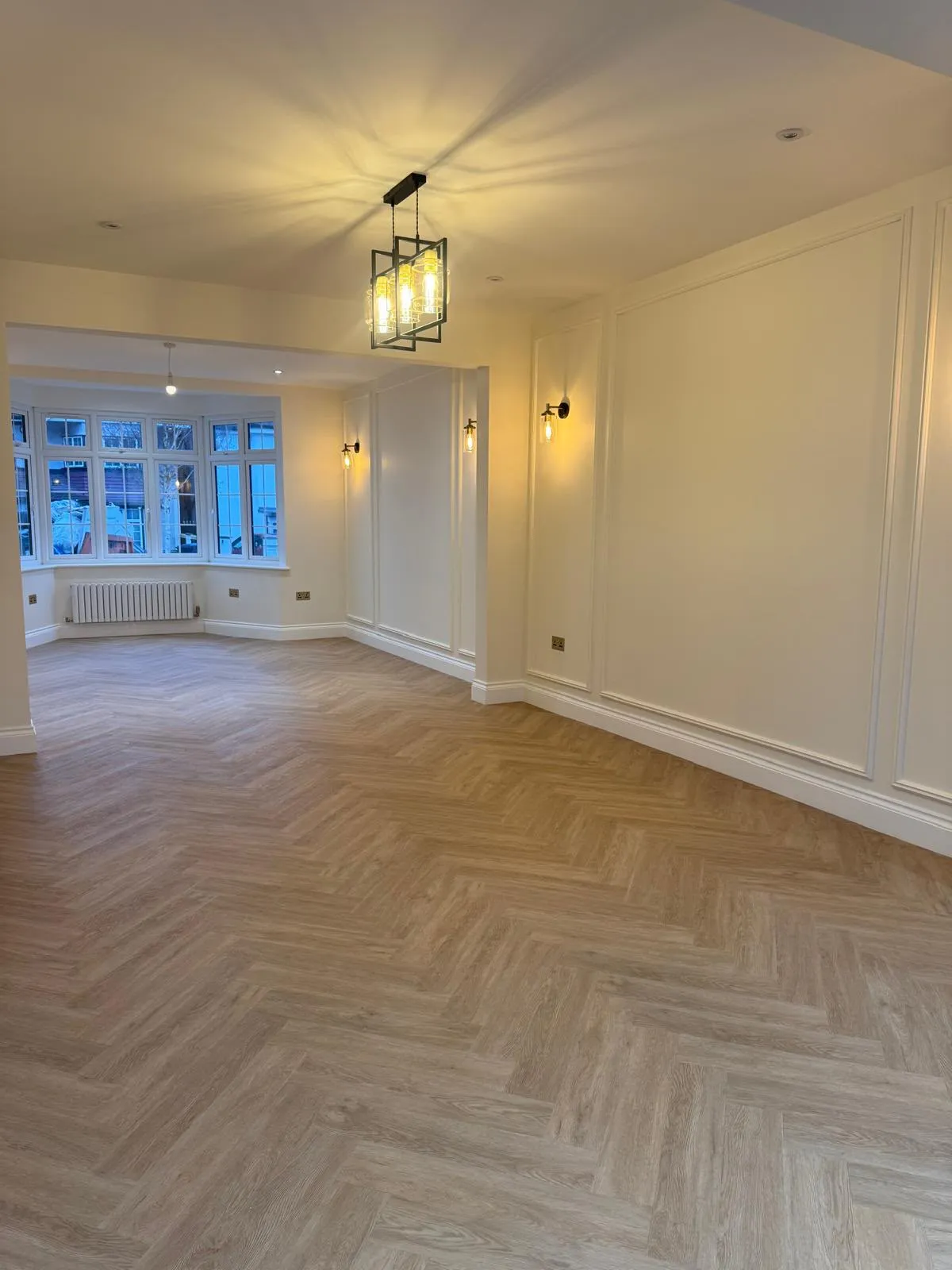 Open-plan living room with bay window, wall panelling and herringbone floor