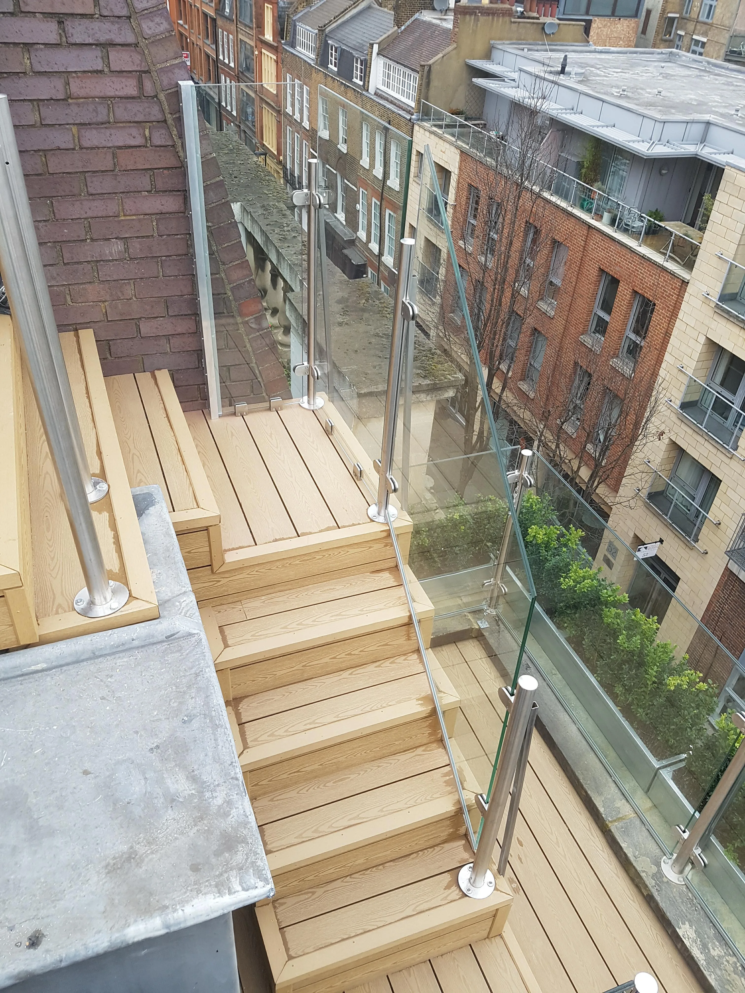 Glass and wooden stairway leading to a rooftop terrace with modern urban view