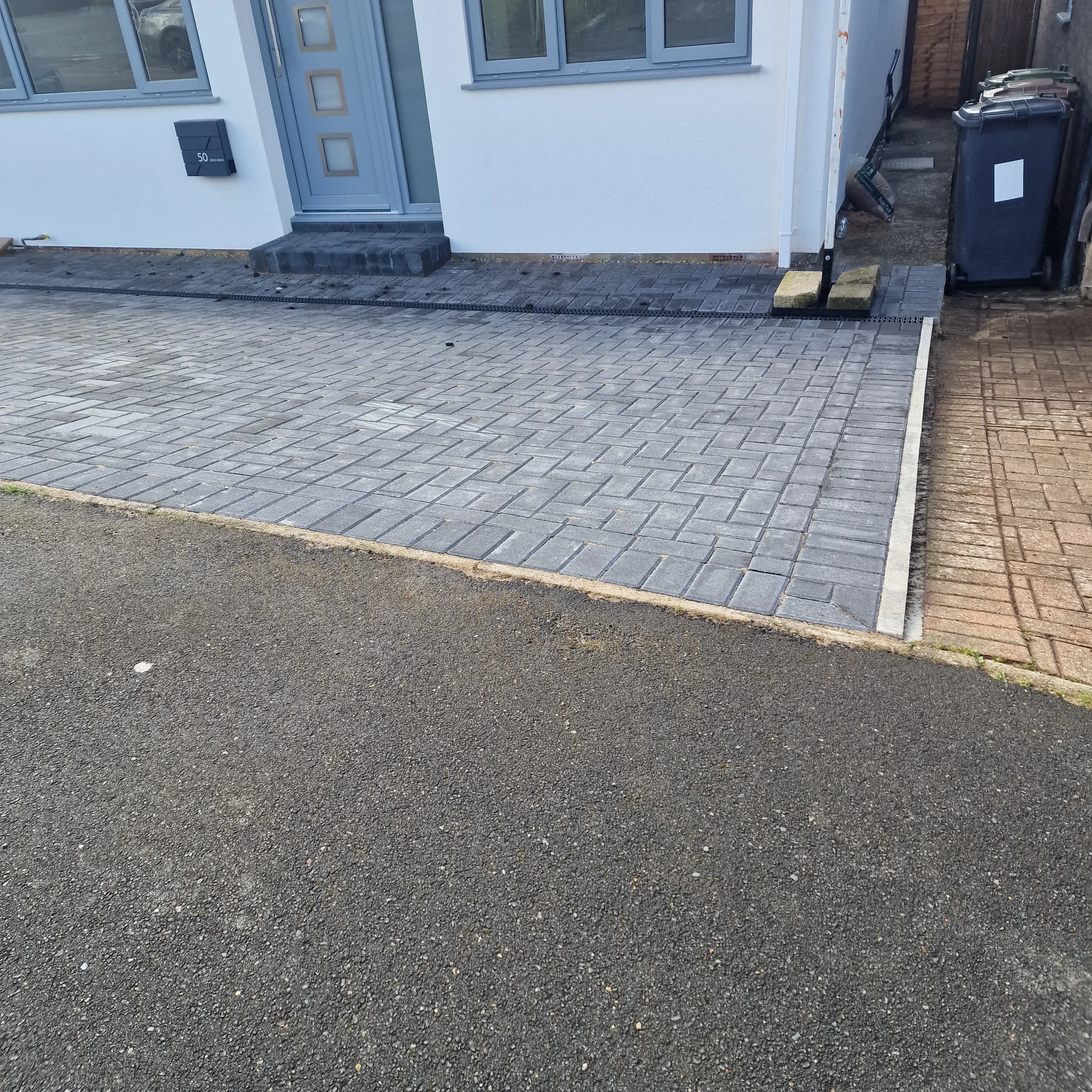 A driveway paved with grey bricks leading to a modern home entrance