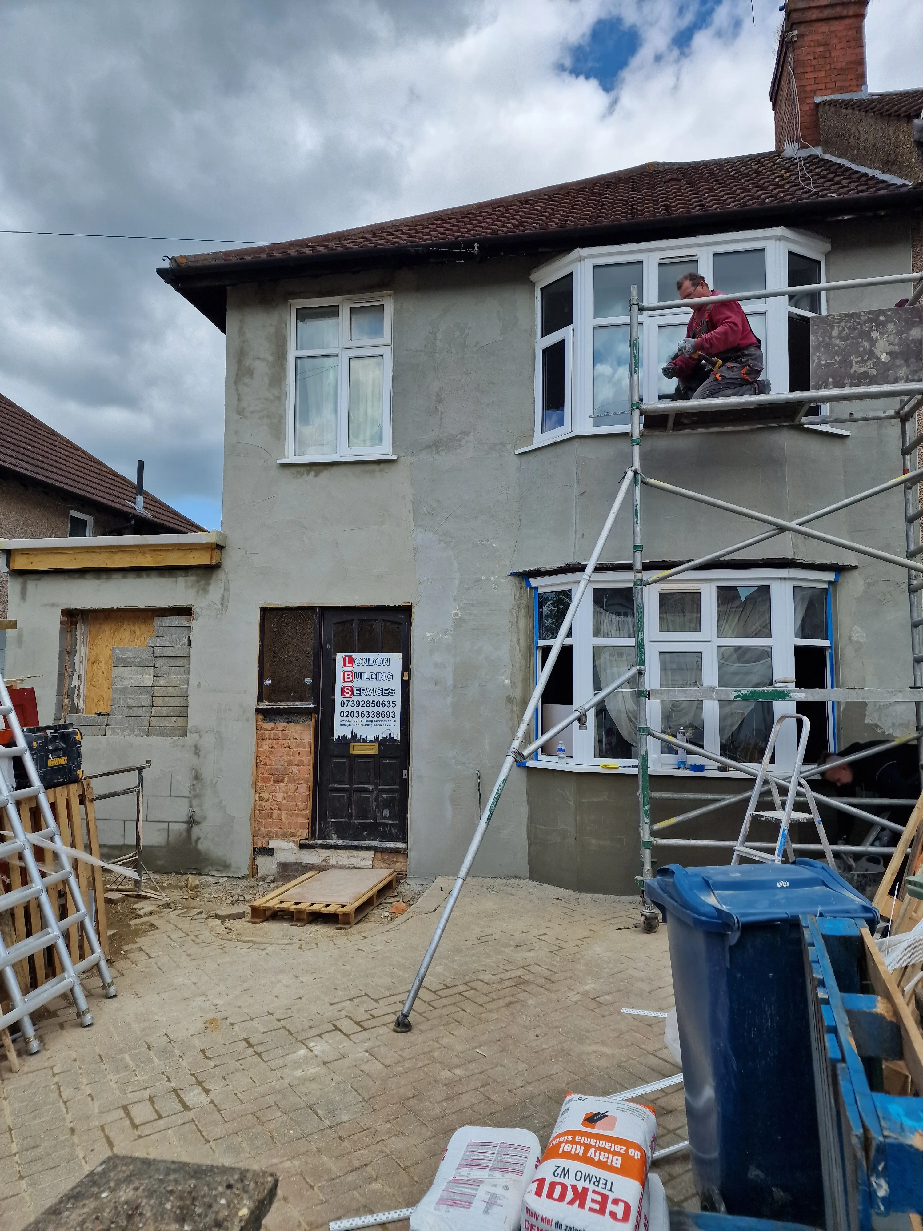 Exterior wall rendering in progress on a residential property with scaffolding and workers