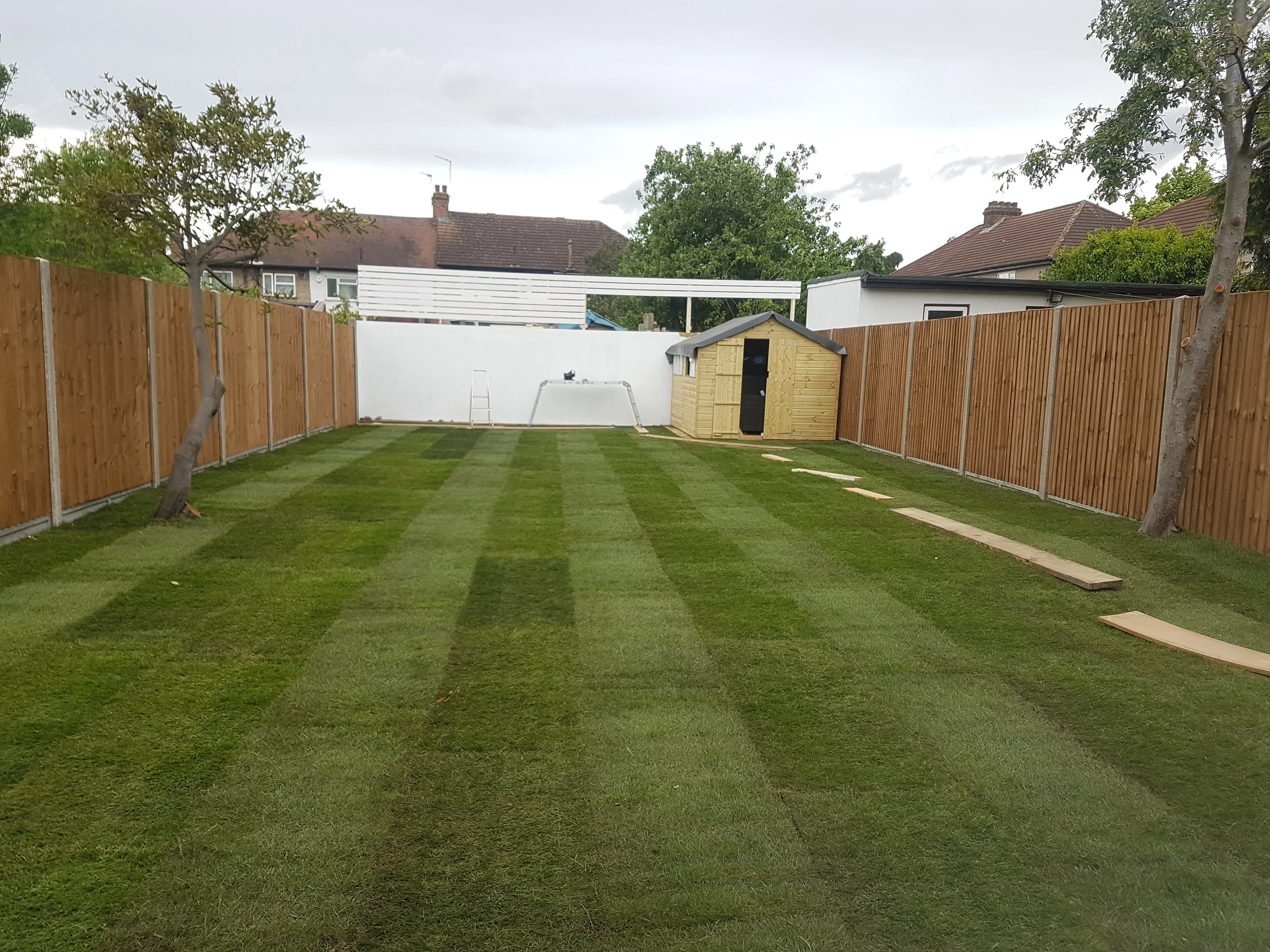 A well-maintained garden landscape with freshly mowed grass, wooden fencing, and a small shed
