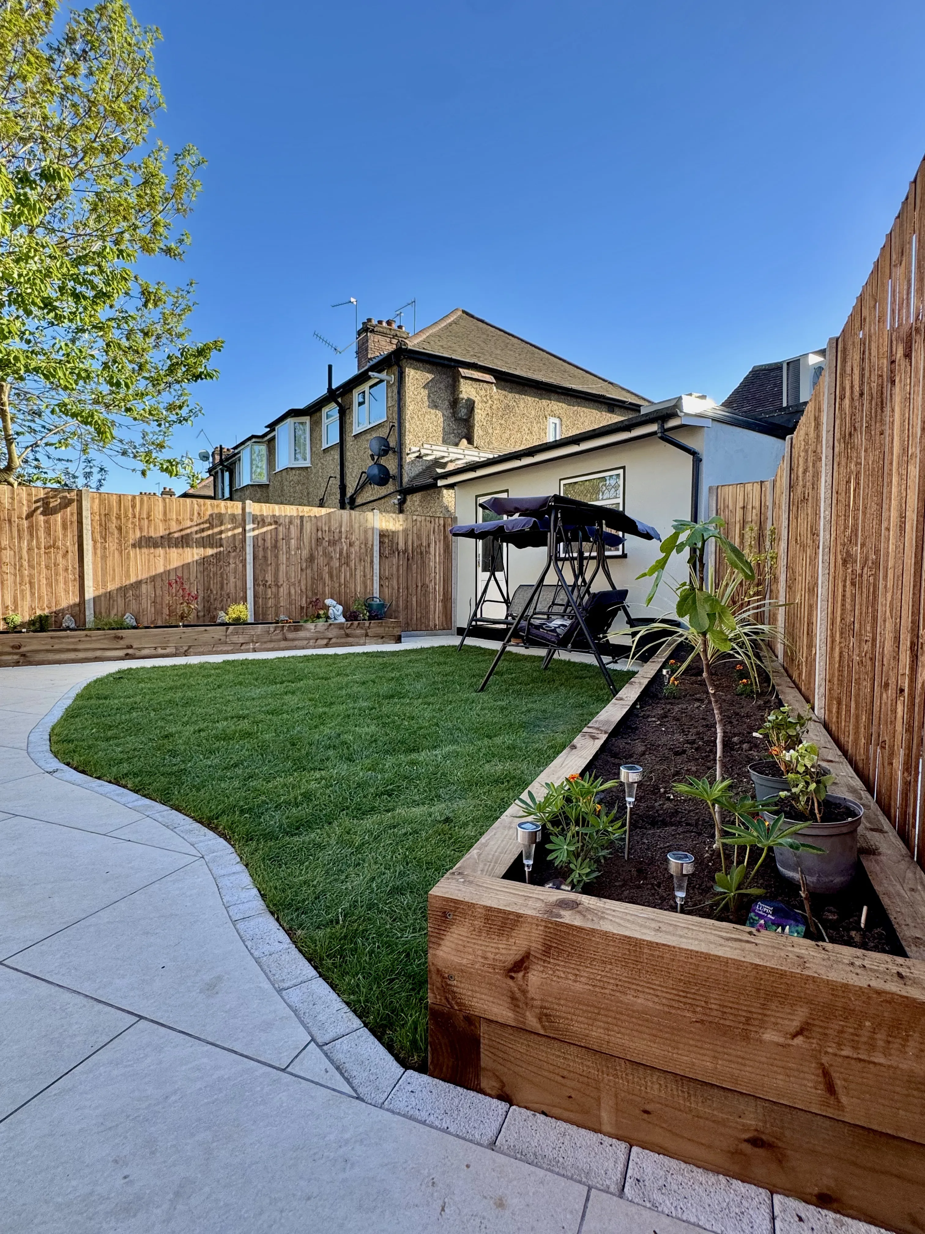 Renovated garden with wooden planters, fresh grass, and a patio area for outdoor dining
