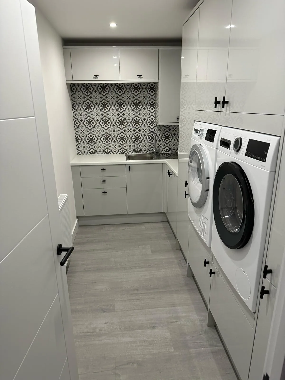 Modern laundry room featuring white cabinetry and patterned backsplash