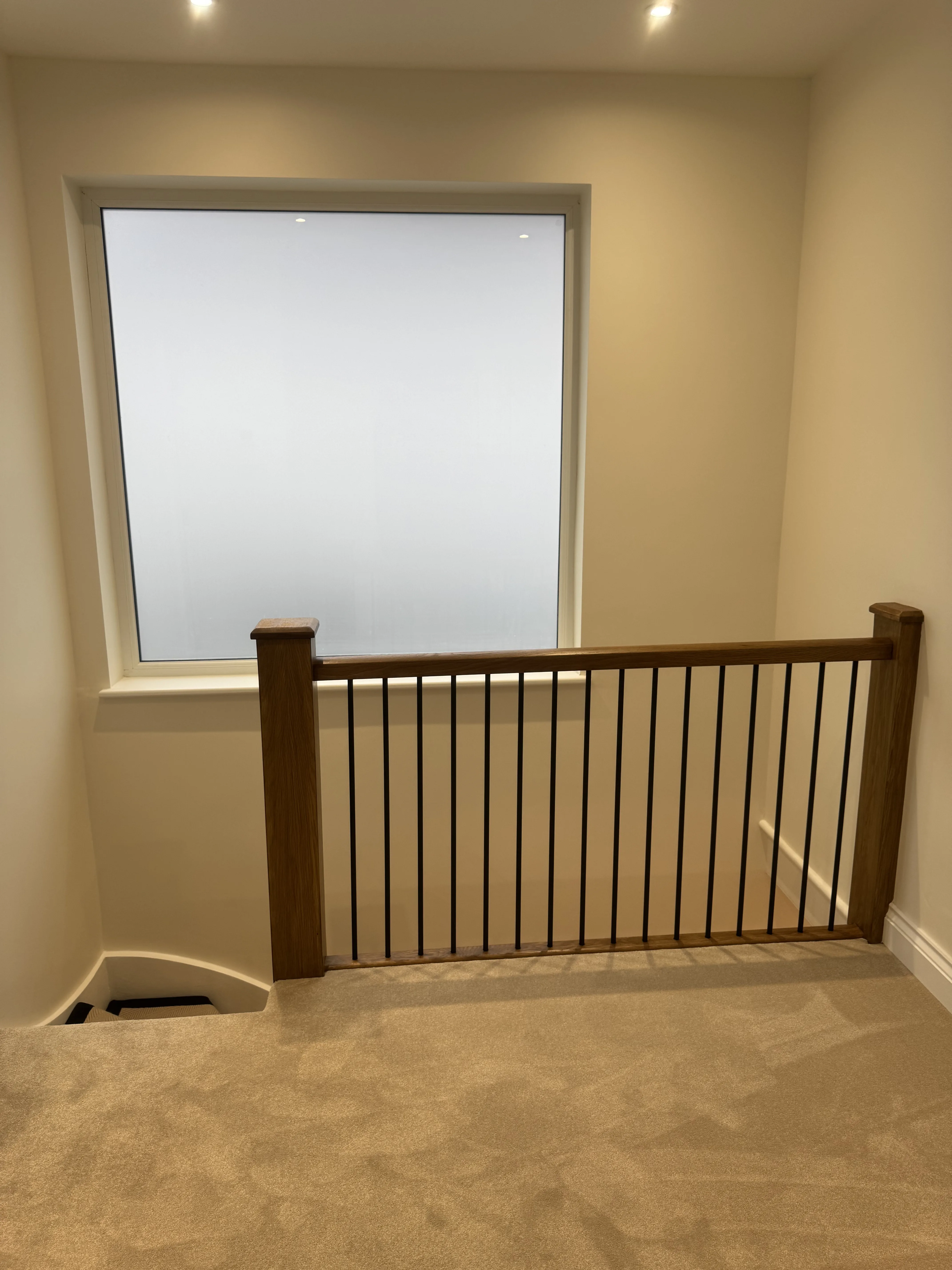 View of a modern stairway railing leading to a large window, featuring neutral colors