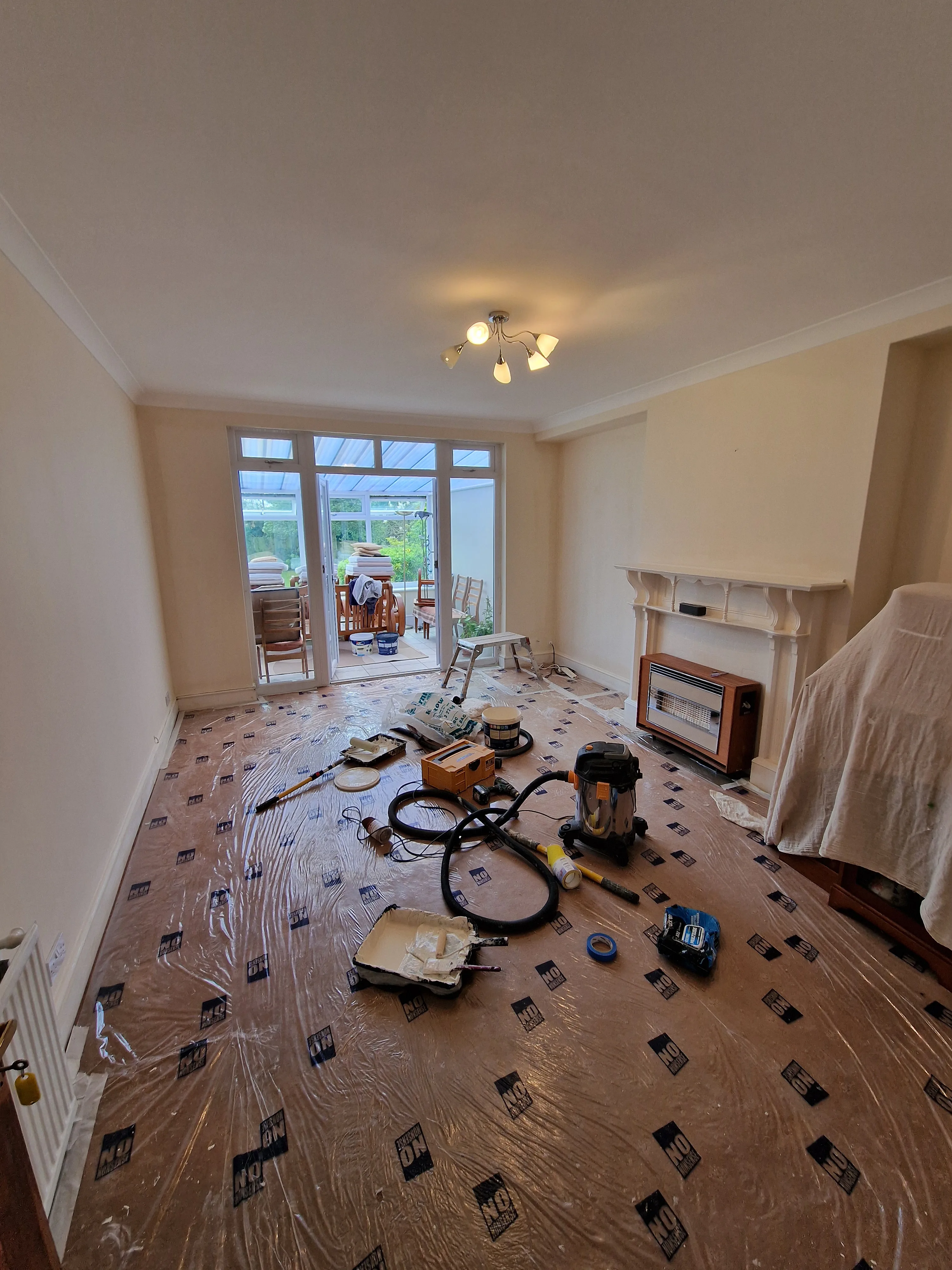 Renovation in progress with tools and plastic covering on the floor in a living room