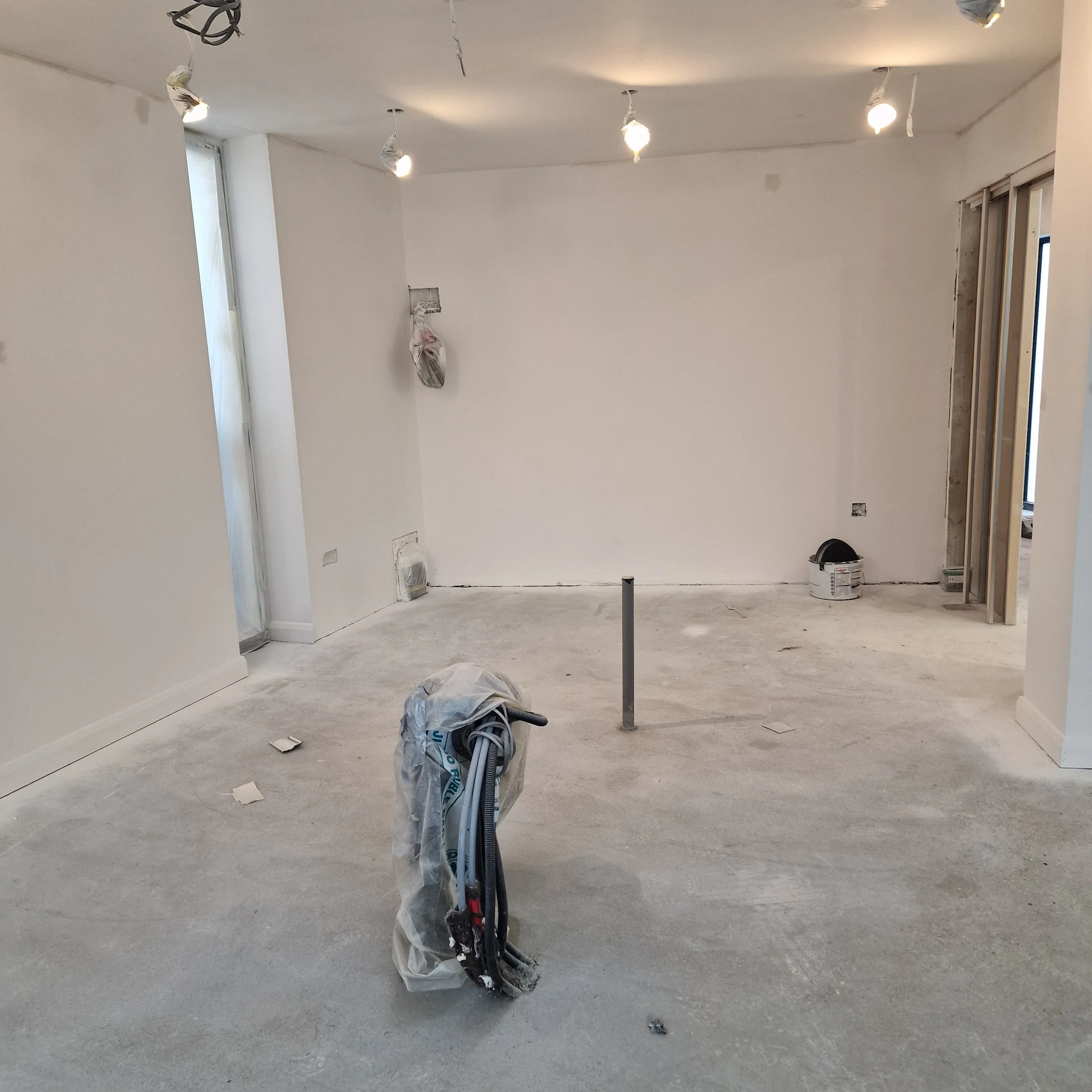 A partially renovated room with a clean concrete floor and construction tools in the center
