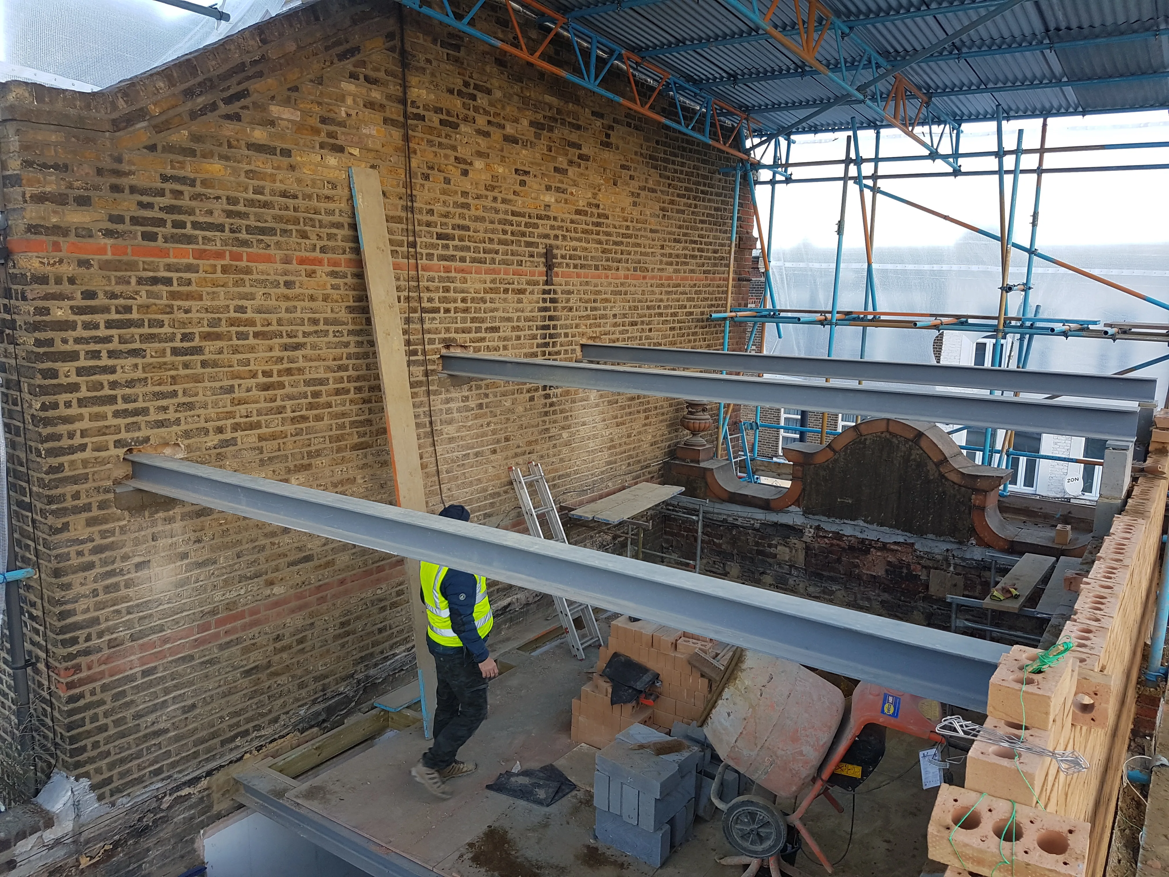 Construction site showing steel beams for a house extension with a worker in safety gear