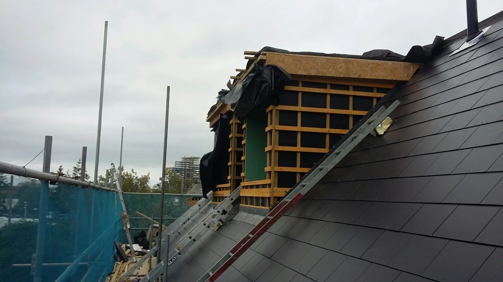 View of a roof construction site showing wooden framing and slate tile installation